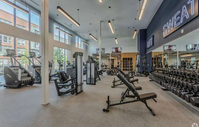 a gym with cardio equipment and weights in a building with large windows