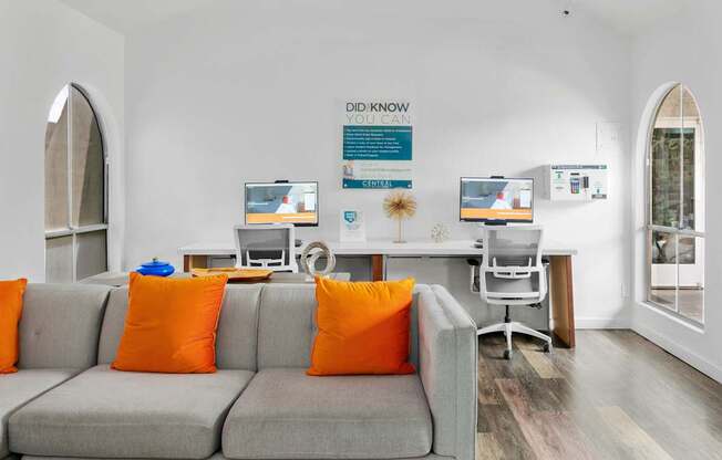 A living room with a grey couch and orange pillows.