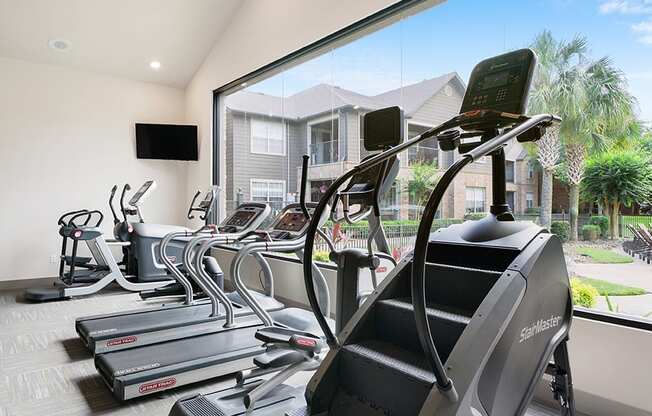 A row of treadmills in a gym with a view of a residential area outside the window.