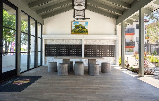 A long black board with white text is in the middle of a room with concrete floors and pillars.
