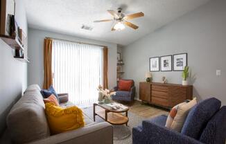 A living room with a grey couch, a blue couch, a wooden coffee table, and a ceiling fan.