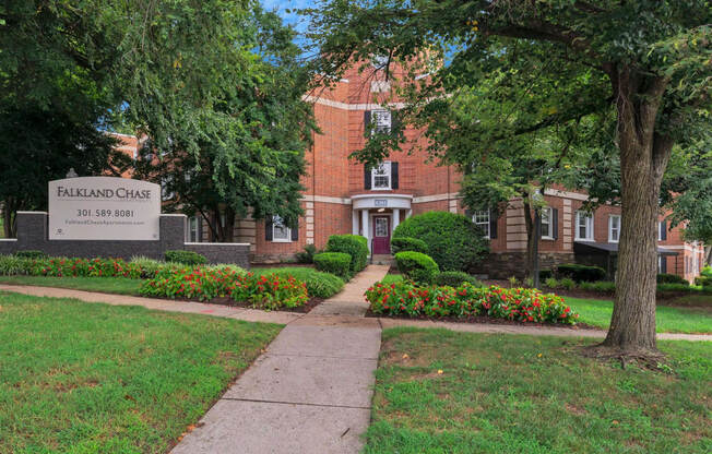 a sidewalk in front of a brick building with trees and flowers