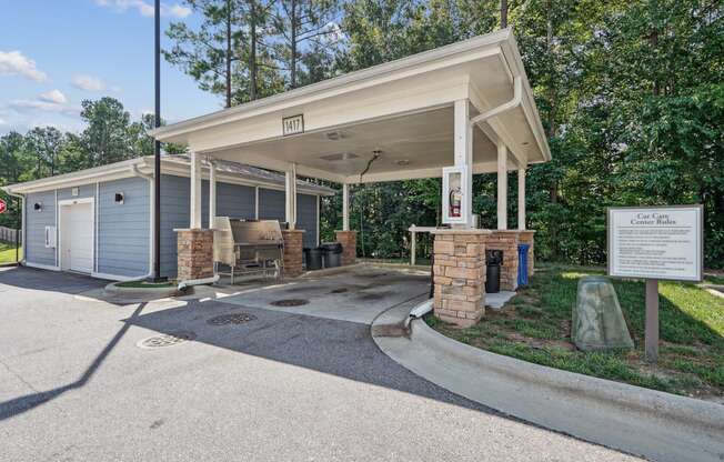 a covered pavilion with a picnic table in front of a parking lot