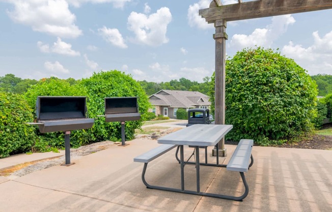 two grills and a picnic table in a park with benches