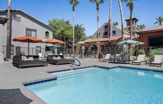 A pool surrounded by palm trees and lounge chairs.