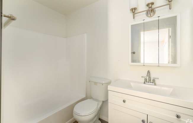 A white bathroom with a toilet, sink, and mirror.