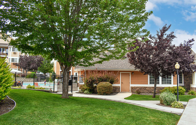 Exterior of community with green grass, trees and a pool in the background.