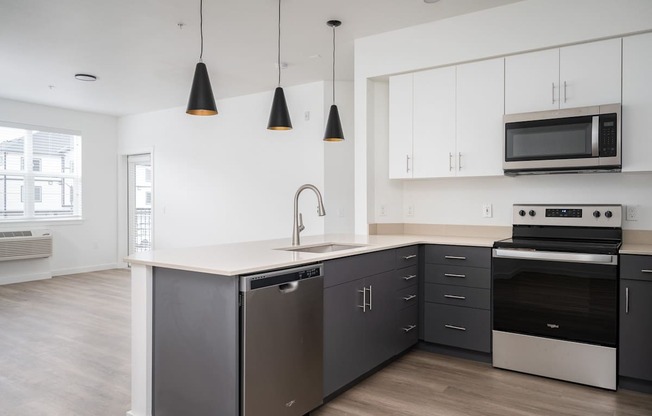 A modern kitchen with a stainless steel dishwasher and oven, a microwave above the stove, and pendant lights hanging from the ceiling.