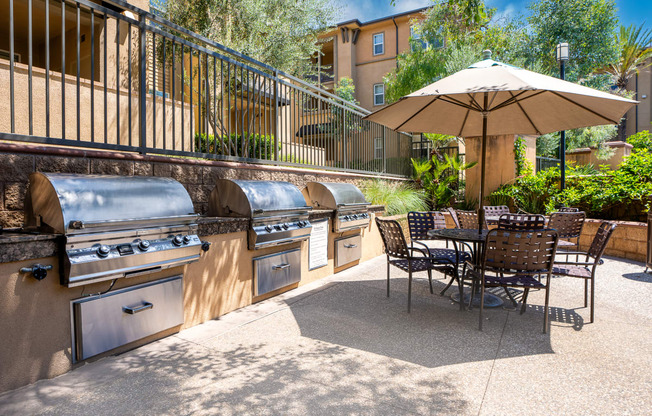 an outdoor patio with barbecue grills and a table with chairs and an umbrella