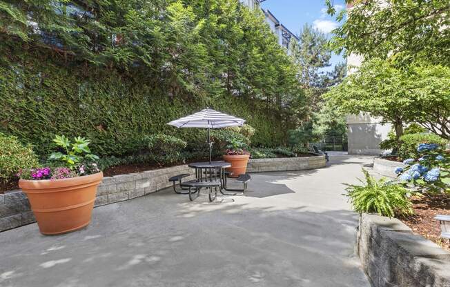 Resident Seating Area in Outdoor Lounge with Well-Landscaped Areas and Shaded Patio Table at Promenade at the Park Apartment Homes, Seattle, WA