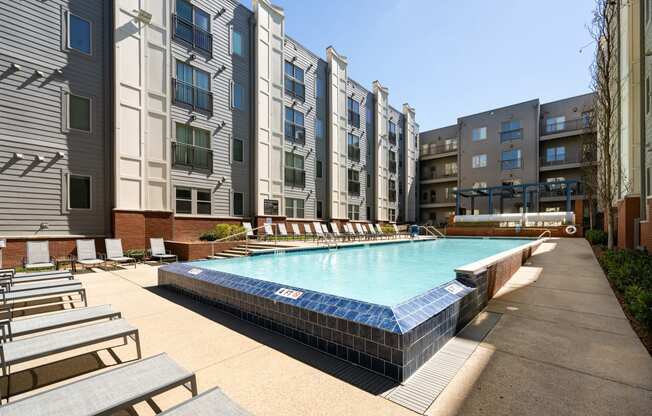 an outdoor pool with lounge chairs in front of an apartment building