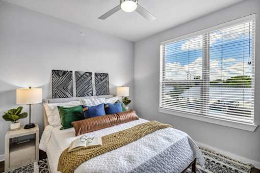 A bedroom with a bed, two lamps, and a window with blinds.