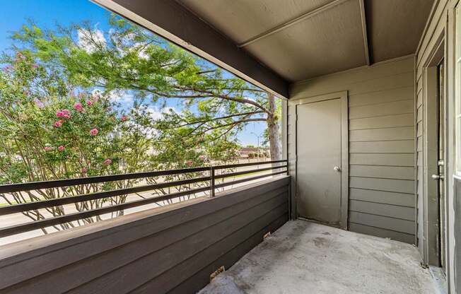 A balcony with a door and a railing with flowers in the background.