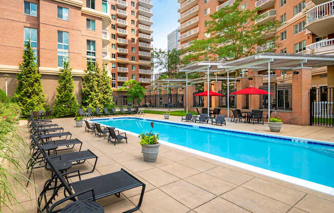 A pool surrounded by chairs and umbrellas in a courtyard.