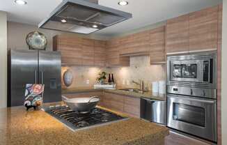 Irvine, CA, Apartments - Astoria at Central Park West - Kitchen with Fisher & Paykel Stainless Steel Appliances, Kitchen Island with Gas Range and Hood, Sandy Granite Countertops, and Custom Craftsman Cabinetry.