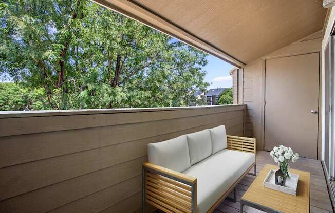 A wooden bench with a white cushion is on a wooden table with a vase of white flowers on it.