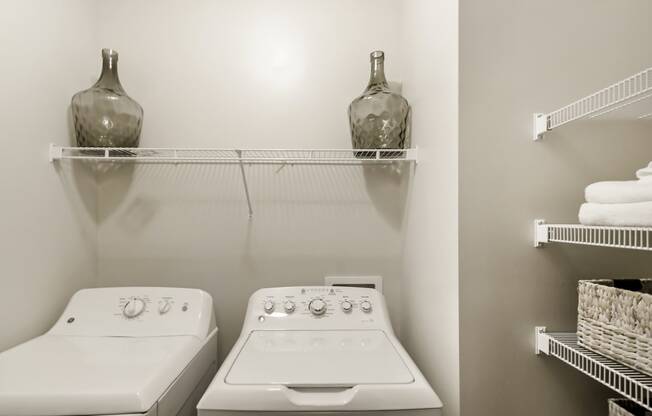 a laundry room with two white appliances and a shelf with a vase on top