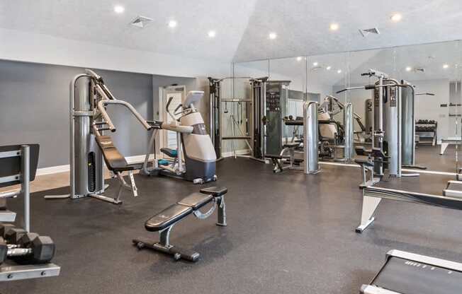 A spacious gym with a variety of equipment including a treadmill, weight bench, and leg press machine at Ridge Crossings Apartments, Alabama