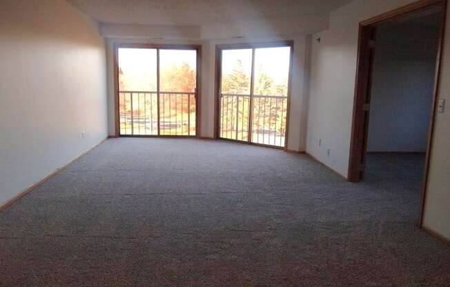 A room with carpeted floor and two sliding glass doors.