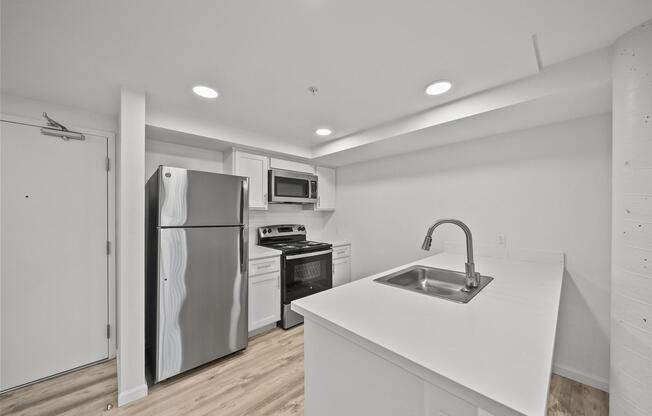 Modern kitchen featuring a stainless steel refrigerator, microwave, and stove, with white cabinets and a sleek countertop. Neutral-colored walls and flooring enhance the spacious feel, complemented by bright overhead lighting.