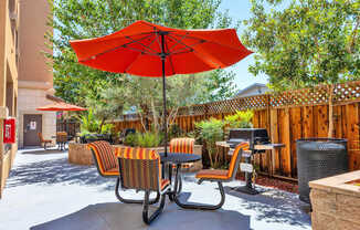 A red umbrella is in the middle of a patio with chairs and a table.