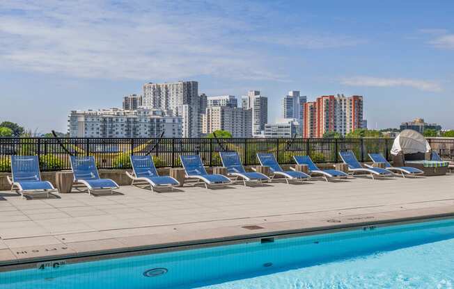 a row of lounge chairs next to a pool with a city in the background