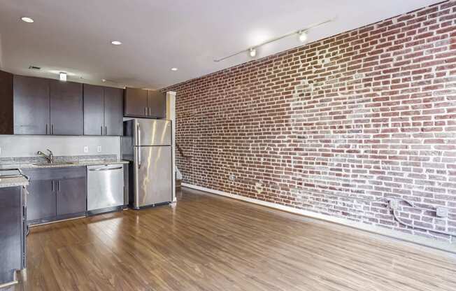 a living room with a brick wall and a kitchen with stainless steel appliances
