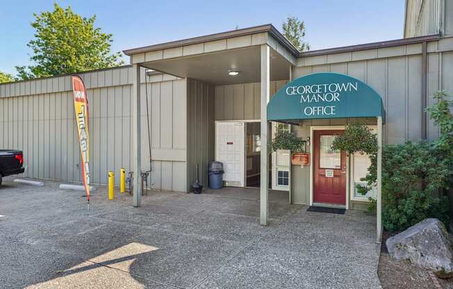 The Georgetown Manor Office is a small building with a red door and a green awning.