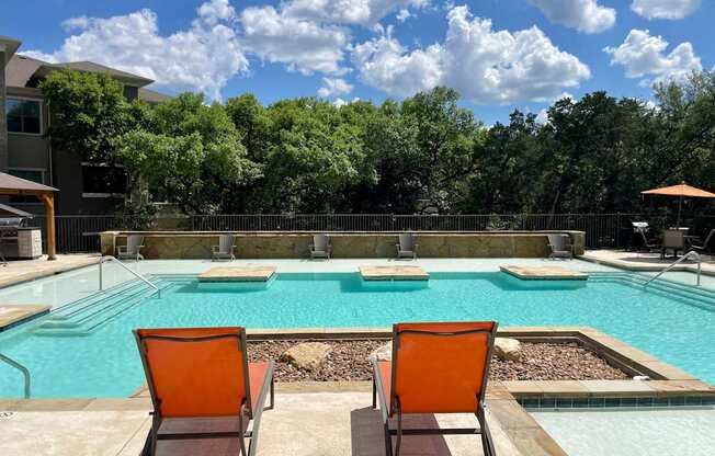 a pool with two orange lounge chairs and a swimming pool with trees in the background