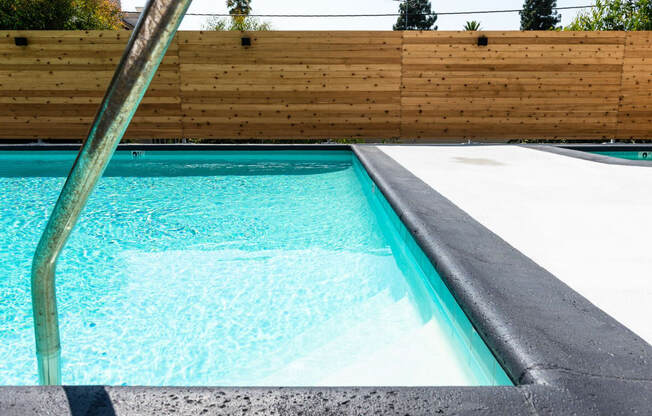 a swimming pool with a concrete coping and a wooden fence