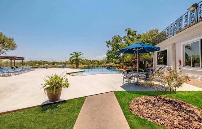 A pool area with a blue umbrella and a concrete walkway.