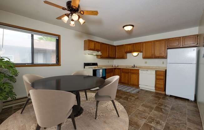 Fargo, ND Gemstone Apartments. a dining area with a table and chairs and a kitchen with a refrigerator and dishwasher. A window fills the room with bright natural light