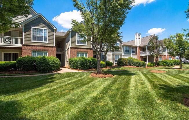 Meticulously maintained grounds with mature trees surround the soft green paint and brick exterior apartment homes at Autumn Park Apartments, Charlotte, NC 28262