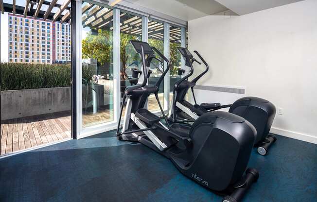 A treadmill and a stationary bike are in a room with a view of a city.