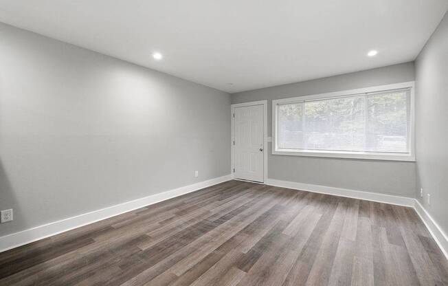 A room with wooden flooring and a window with blinds.