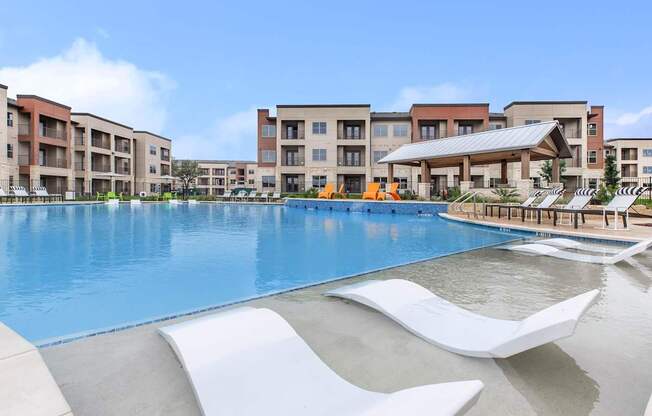 A large swimming pool with lounge chairs in front of apartment buildings.