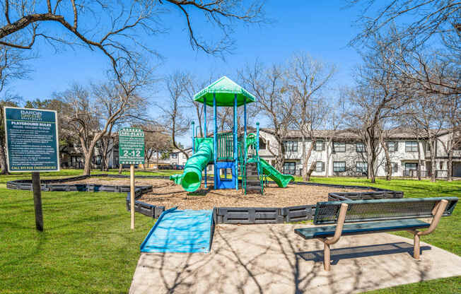 a playground with a green slide and benches in a park