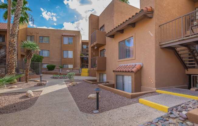 A courtyard with a building in the background and a palm tree to the left.