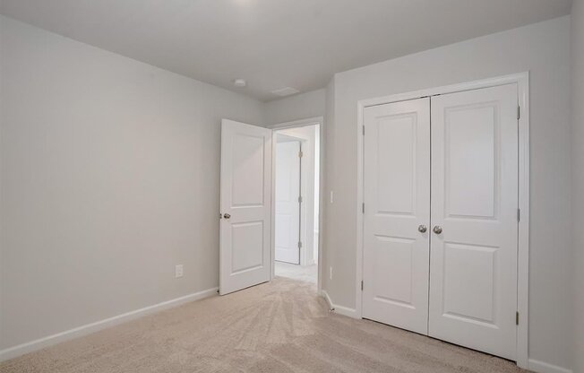 A room with white walls and carpeted floor with two white doors.