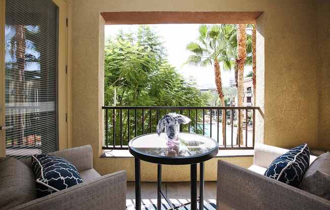 A balcony with a table and two chairs overlooking a lush green area at The Kitt at Warner Center Apartments, California
