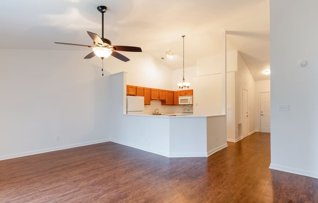 an empty living room with a ceiling fan and a kitchen