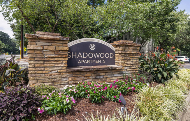 the shadwood apartments sign on a stone wall with plants