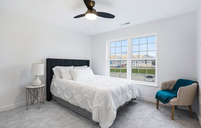 A bedroom with a large bed, a chair, and a ceiling fan at Meadowbrooke Apartment Homes in Kentwood, MI 49512