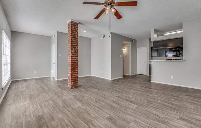 an empty living room with a ceiling fan and a kitchen