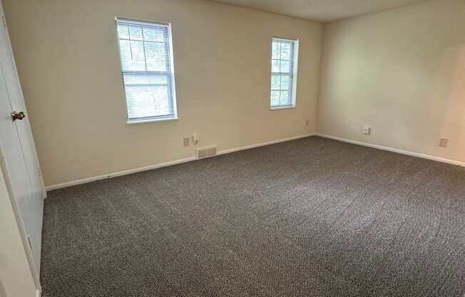 A room with carpeted floor and two windows.