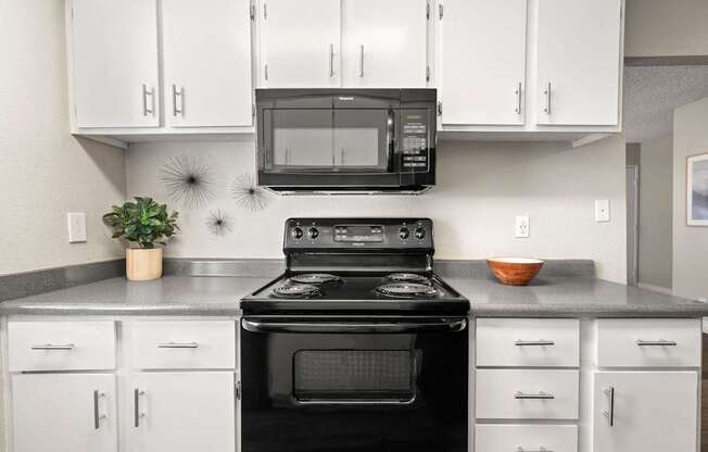 A black stove top oven sits in a kitchen with white cabinets.