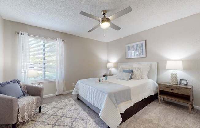 A bedroom with a bed, chair, and a ceiling fan.