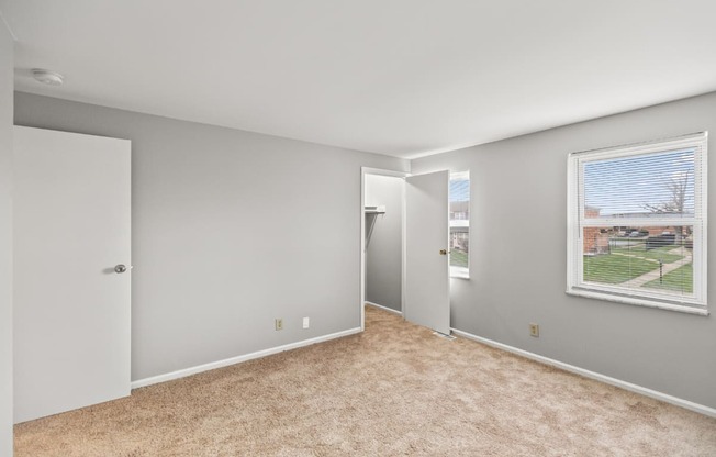 A room with carpeted floor and a window showing a view of a residential area.