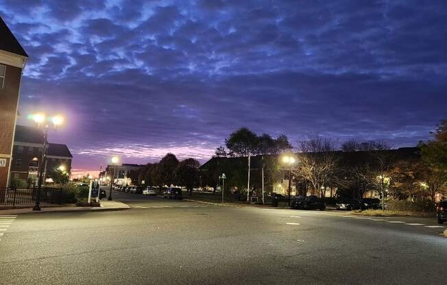 A street view of a parking lot at dusk with street lights on.
