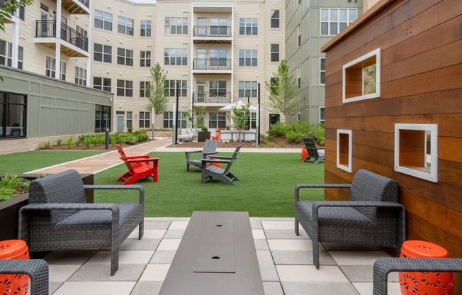 an outdoor lounge area with chairs and tables in front of an apartment building